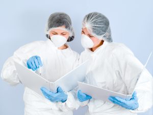 Two lab technicians in scrubs read out of binders